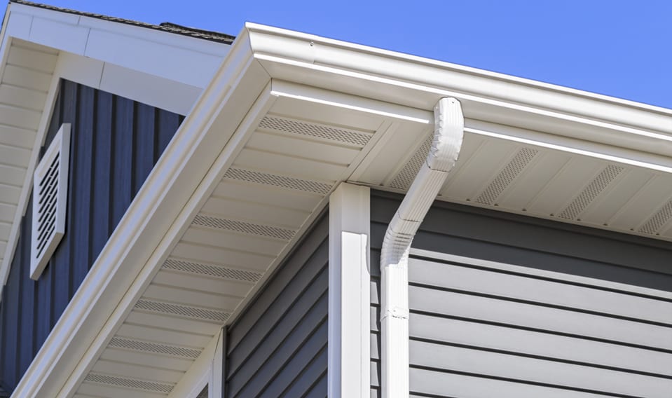 A close-up image of a home with gray lap siding, and a white gutter system with downspout.