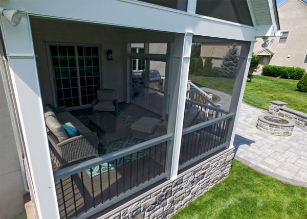 The exterior of a screened in porch. It features large screens for outdoor views and a comfortable interior setup with cushioned patio furniture.