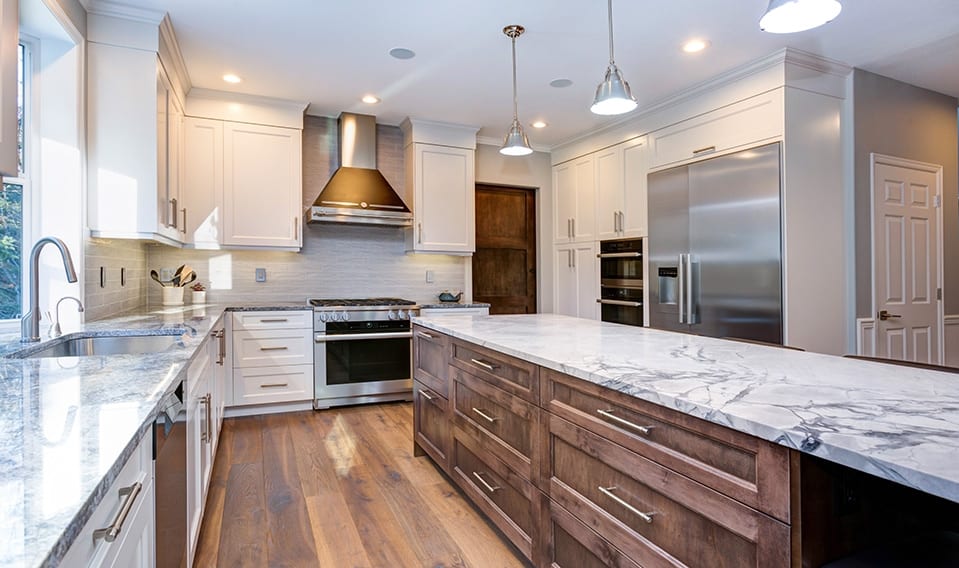 A beautifully updated kitchen with marble countertops, hardwood floors, pendant lighting, and a mix of white and dark wood cabinetry. 