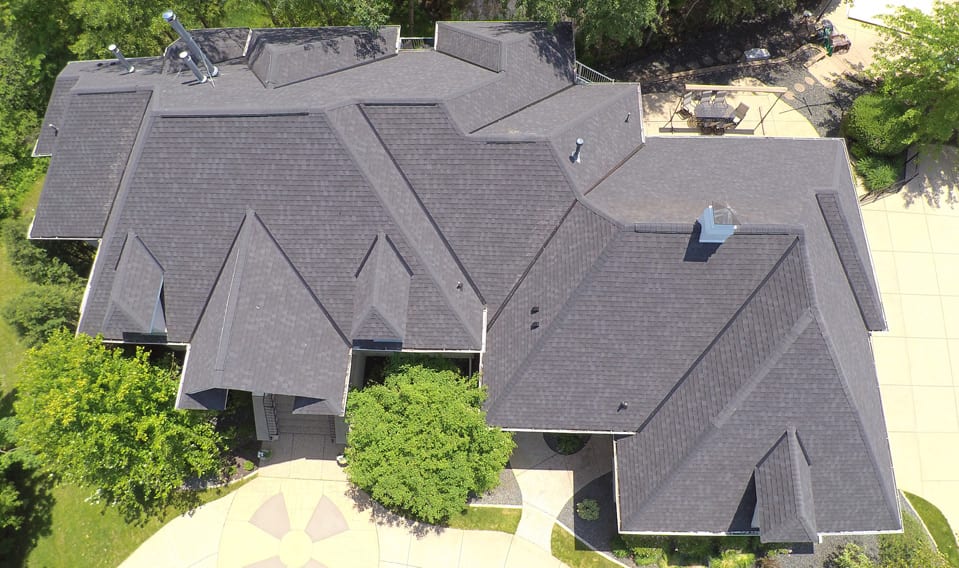 An aerial view of a very large home with a new, gray asphalt shingle roofing system.