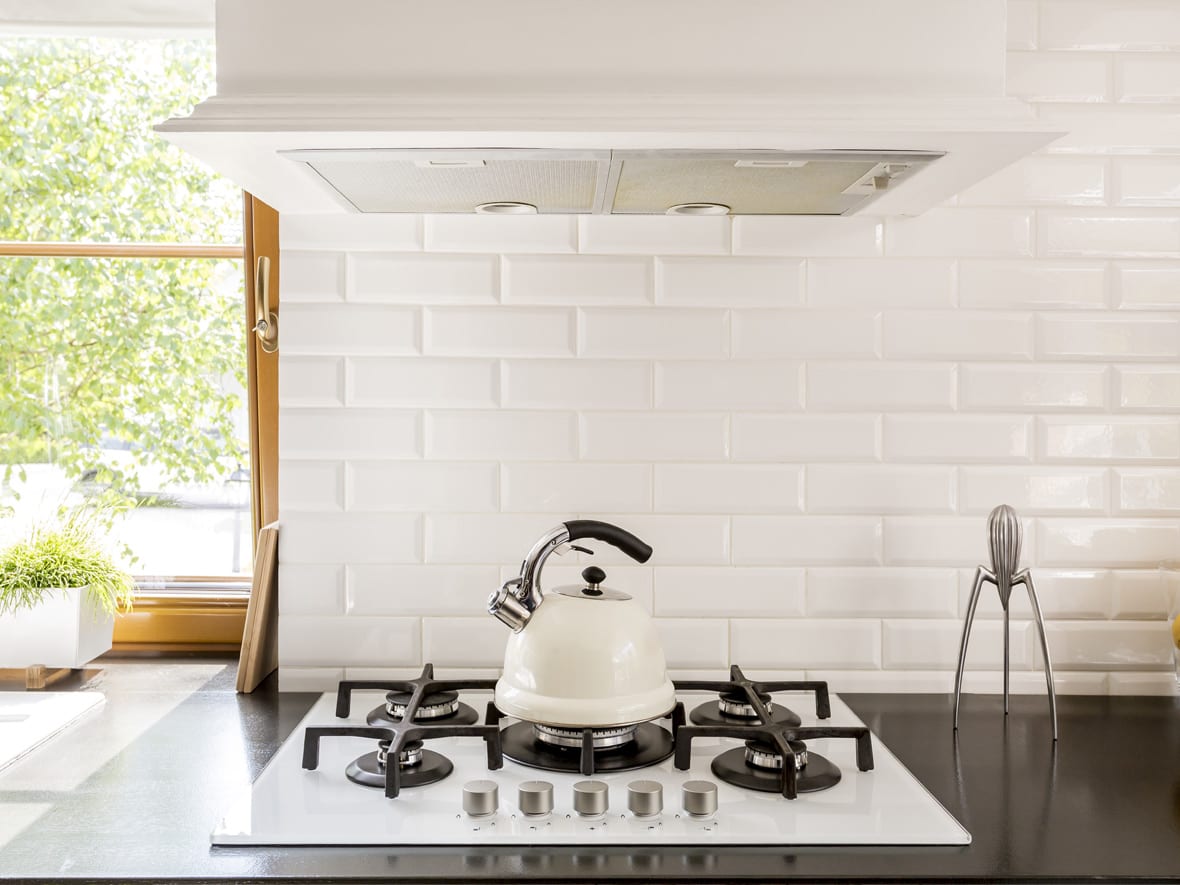 A tea kettle sits on a modern, build-in gas stove with spider burners. A white subway tile backsplash is in the background.